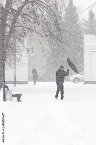Bad weather in a city: a heavy snowfall and blizzard in winter. Unidentified male pedestrian hiding from the snow under umbrella. Heavy gust of wind tears the umbrella out of his hands, vertical