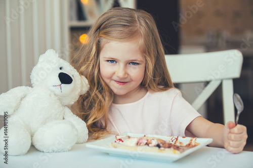 Portrait of beautiful little girl with a Teddy bear in a cafe eating ice cream .Happy moments photo