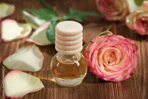 Rose essential oil in glass bottle on wooden background