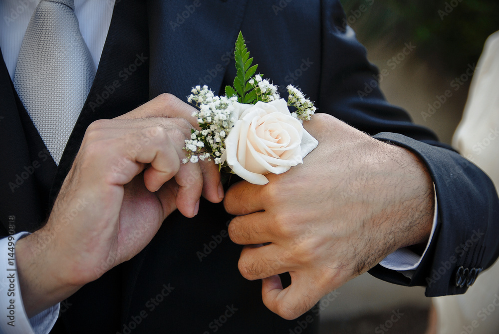 Dettaglio di abito da sposo in cui lo sposo si sistema il fiore nella giacca