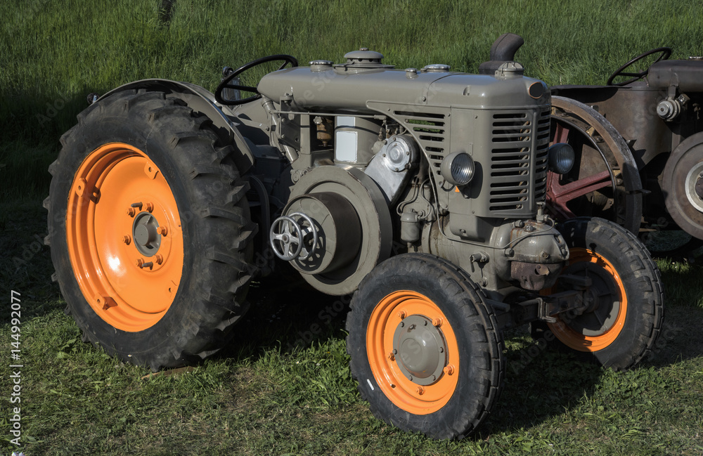 An old orange and green retro tractor in a field. An old orange and green retro tractor in a field.