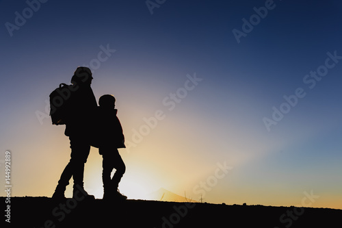 Silhouettes of father and son hiking in sunset mountains