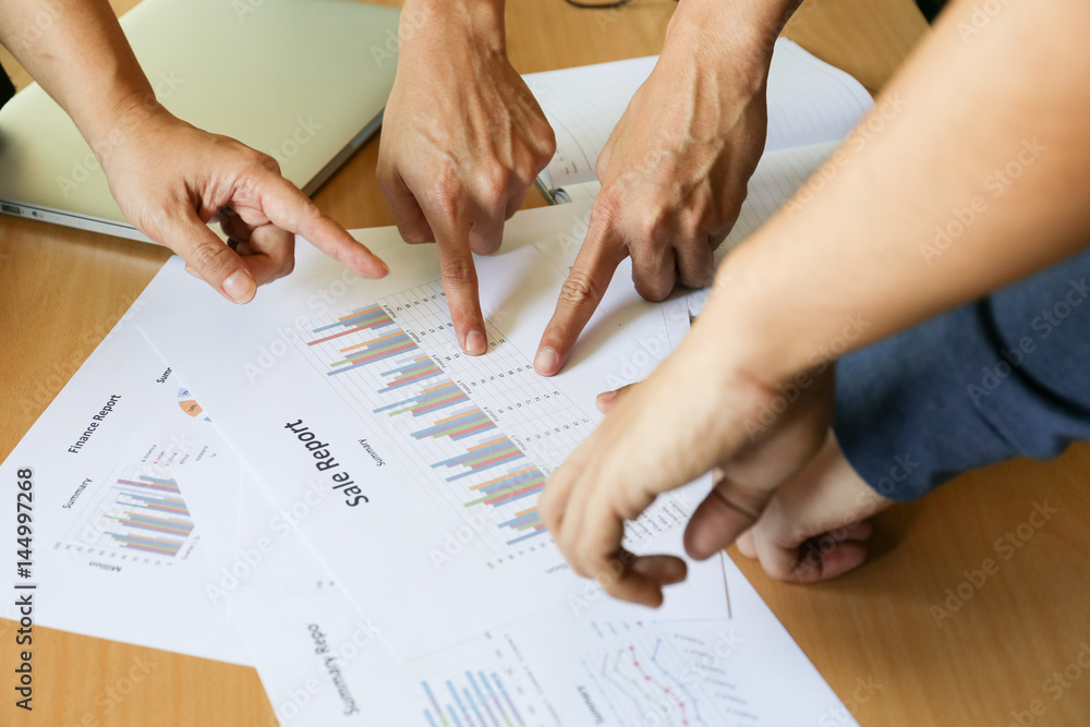 many fingers point at sale report charts paper on wooden desk many fingers point at sale report charts paper on wooden desk