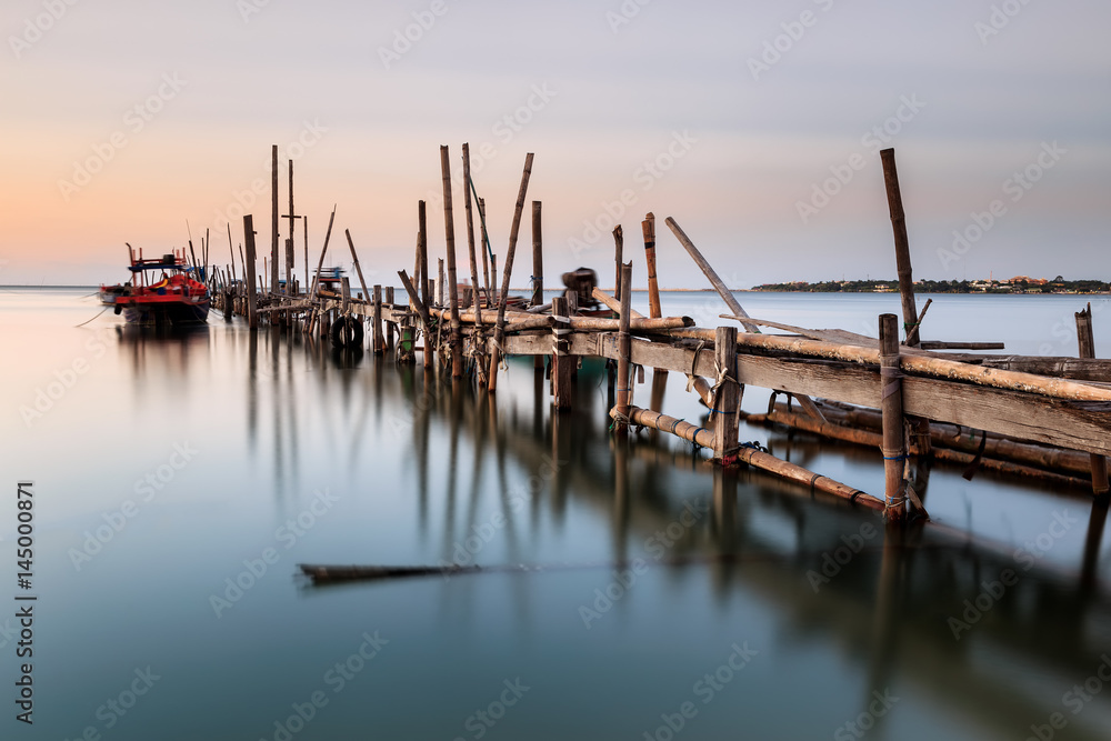 Fototapeta premium Old wood bridge for small fishing boat in the sea with sunset 