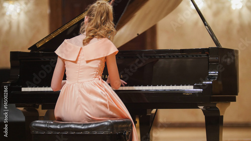 Photos Close up view of cute teenager girl plays piano in the concert hall at scene