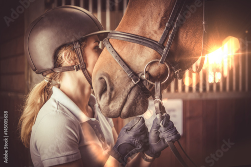 Young women kissing her horse in barn