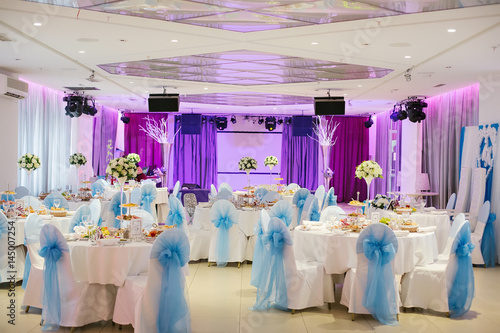 Served tables with a white tablecloth and chairs with white covers, decorated with blue bows