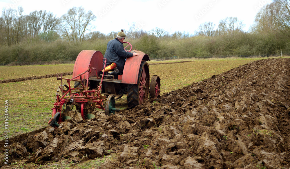Naklejka premium Vintage red International 1930's tractor ploughing field. 