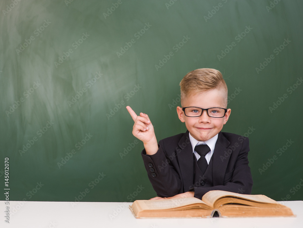 Boy in a suit points on empty green chalkboard Boy in a suit points on empty green chalkboard
