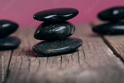 Black stone treatment. Spa and wellness concept. One pink flower on a wooden table and pink background. Lovely flowers. Festive greeting card. Pastel color.. Spring.