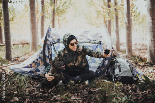 Man backpacker in the mountain with his camping tent and his French bulldog dog