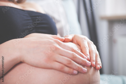 Pregnant girl holding hands in heart shape on belly at home