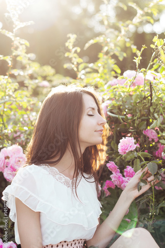 Девушка с длинными волосами сидит рядом с розовыми розами в саду 