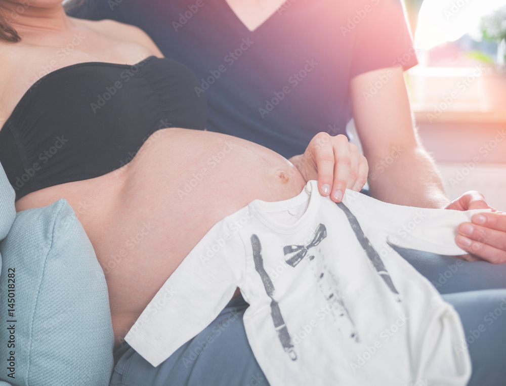 Φωτογραφία Close up of pregnant belly with clothes for unborn baby parents at home