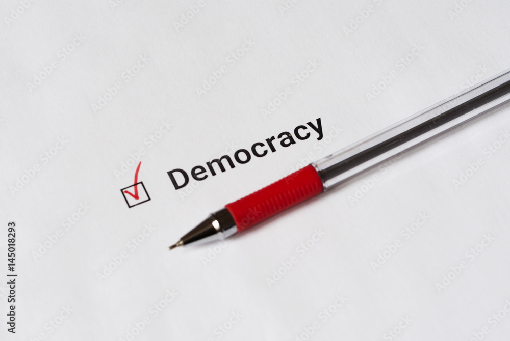 Questionnaire. Red pen and the inscription Democracy with check mark on the white paper Questionnaire. Red pen and the inscription Democracy with check mark on the white paper