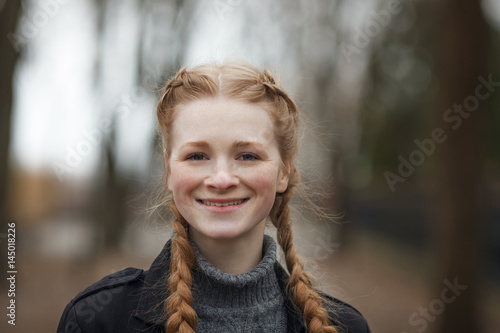 Close up emotional portrait of happy beautiful woman with red braids hair and natural makeup wearing black jeans trench grey sweater enjoying her life in spring city park.