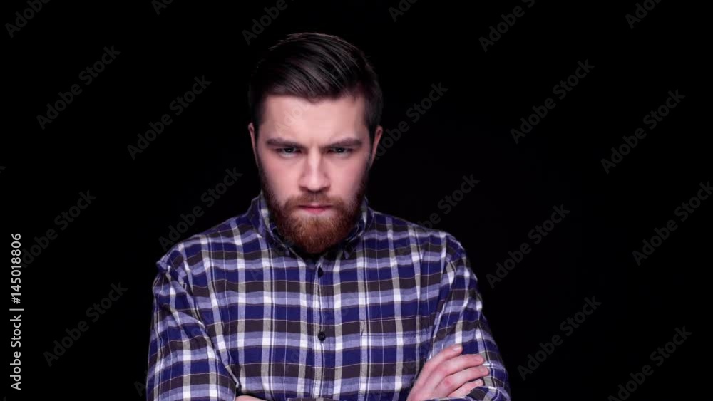 Angry displeased frowning young man looking at camera with arms folded isolated over black Angry displeased frowning young man looking at camera with arms folded isolated over black