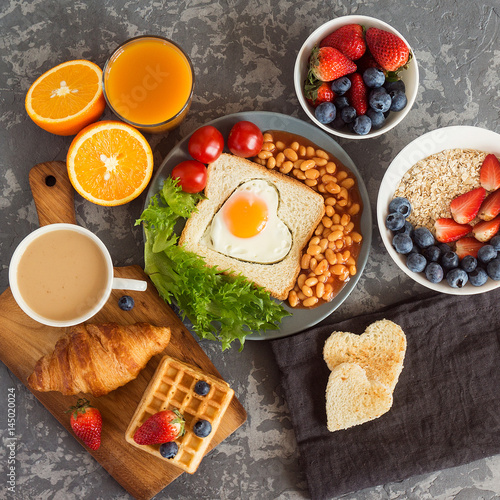 English breakfast: fried egg, beans and toast on a plate with tomatoes cherry, salad, juice, berries and croissant