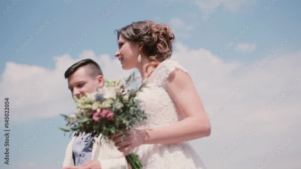 Beautiful bride and handsome groom walk in a park in summertime. White wedding dress and gown, hair-do. Steadicam shot. Beautiful bride and handsome groom walk in a park in summertime. White wedding dress and gown, hair-do. Steadicam shot.