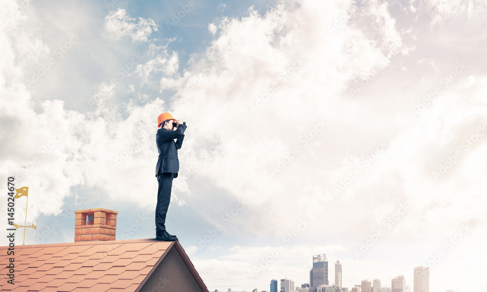 Engineer man standing on roof and looking in binoculars. Mixed m Engineer man standing on roof and looking in binoculars. Mixed m