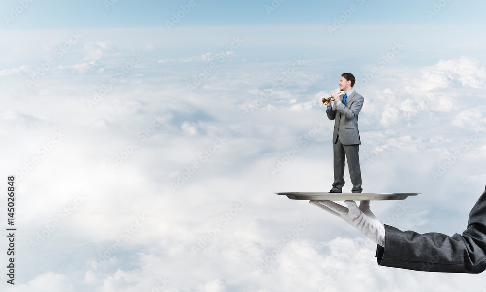 Businessman on metal tray playing fife against blue sky background Businessman on metal tray playing fife against blue sky background