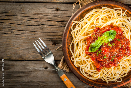 Italian cuisine. Lunch or dinner. A serving of spaghetti pasta with tomato marinara sauce and basil on a dark wooden table. Copy space top view
