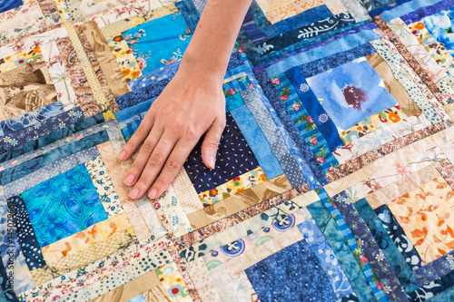 The caucasian female hand touching a color patchwork quilt with blue geometry pattern. Part of Colorful Scrappy blanket close up. dream concept