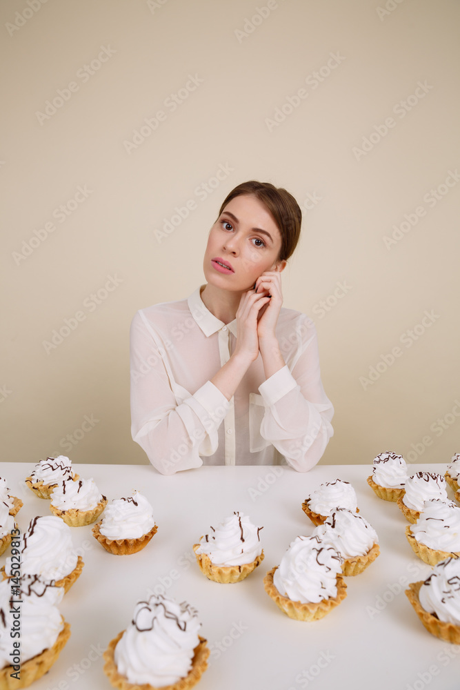 Beautiful young woman sitting at the table with cupcakes Beautiful young woman sitting at the table with cupcakes