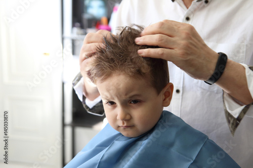 peluquero poniendo gomina a niño pequeño en la peluquería