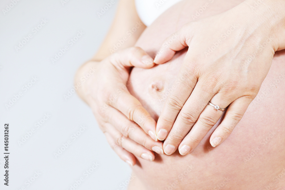 Pregnant woman with shaping heart on her belly with her hands, on grey background, unrecognizable person. Pregnant woman with shaping heart on her belly with her hands, on grey background, unrecognizable person.