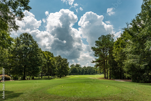 View down a golf fairway lined with trees and dramatic clouds