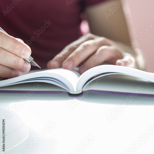 Closeup of a male hand writing on notepad with silver pen