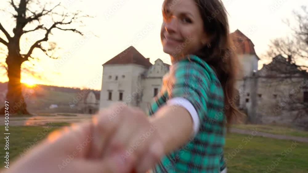Follow me - happy young woman pulling guy's hand against the background of an old castle