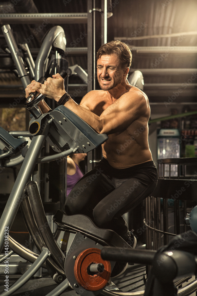 Fototapeta premium Shirtless male athlete exercising on ab coaster gym machine
