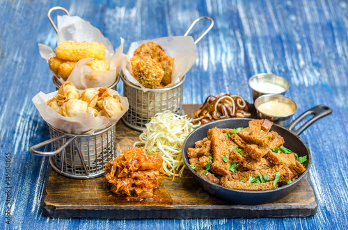 A set of snacks for beer. Chicken sticks in batter, cheese, pork ears, toasts, sauces and cabbage on a wooden board