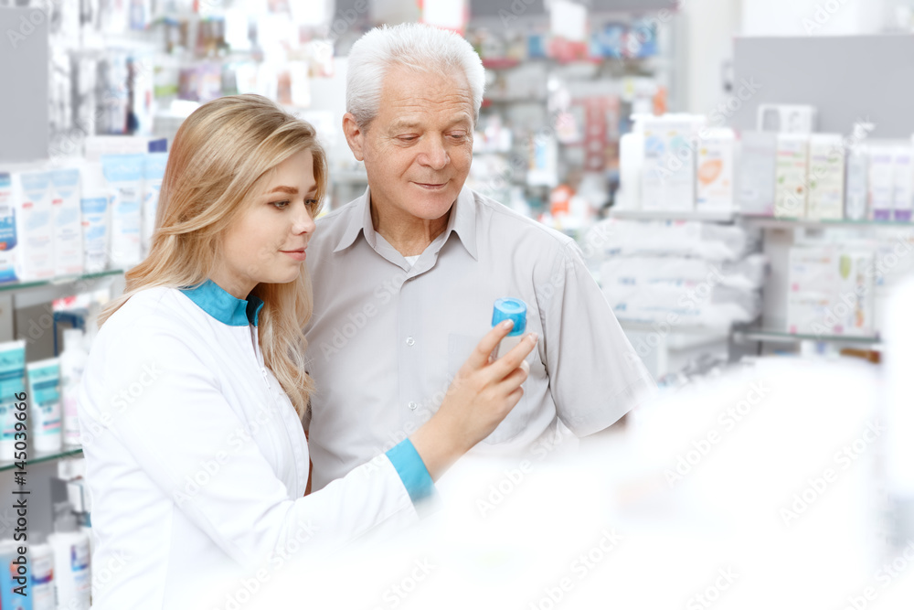 Fototapeta premium Young female pharmacist helping an elderly customer