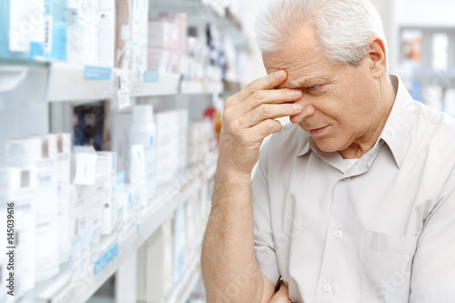 Senior man having a headache standing in the pharmacy store