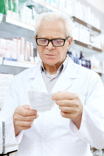 Senior male chemist reading medication prescription working at the drugstore