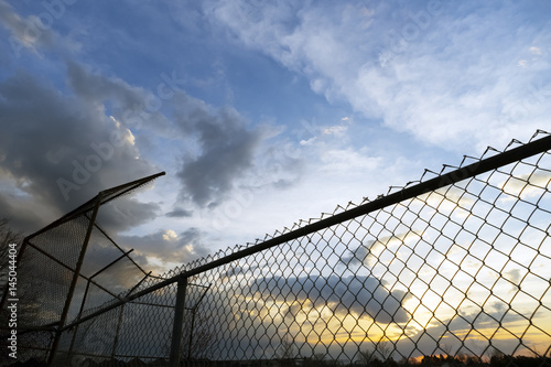Empty community baseball diamond and fence in silhouette against a sunset sky at dusk © Rachel Lerch