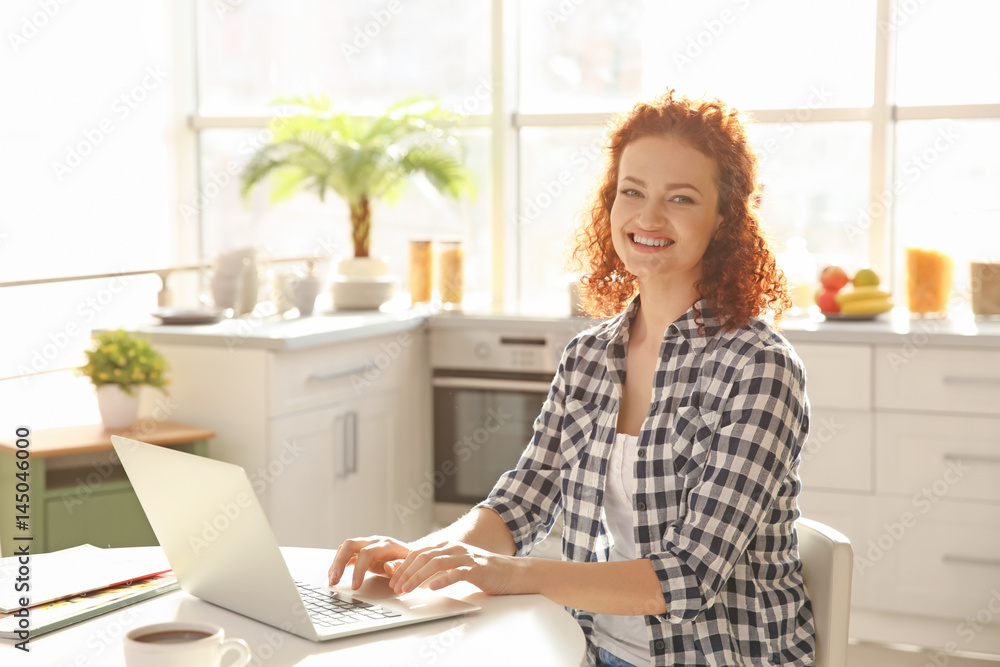 Beautiful young woman sitting at table and using laptop Beautiful young woman sitting at table and using laptop