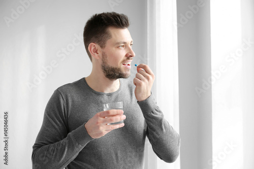 Slika na platnu Handsome young man taking pill at home