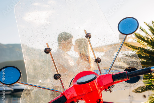 A red retro moped parked at the marina. In Budva, Montenegro. Silhouette of a kissing couple through a glass with raindrops.