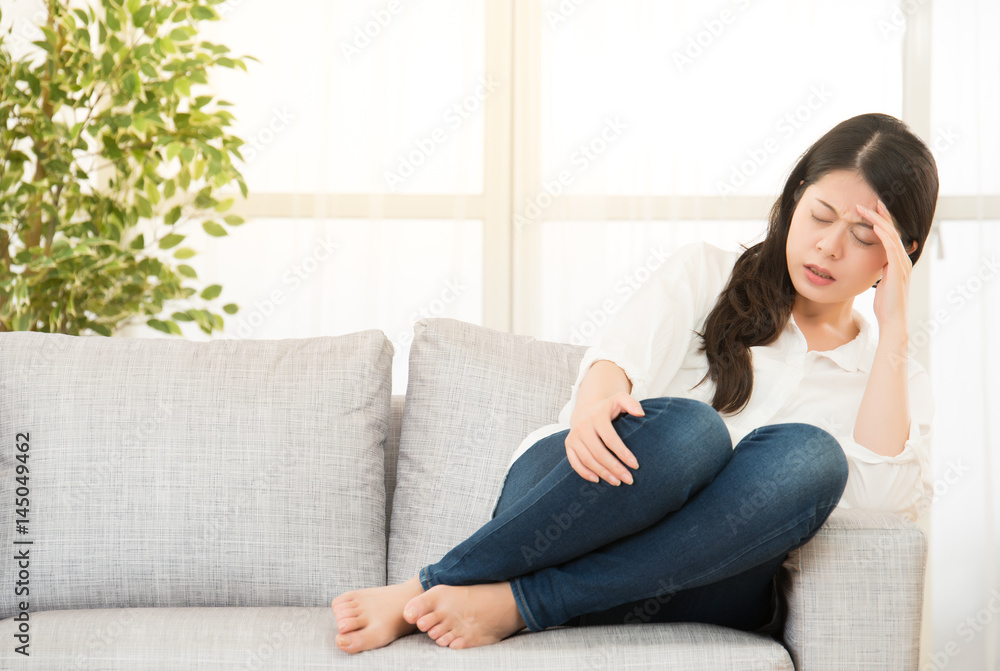 woman suffering headache sitting on sofa woman suffering headache sitting on sofa