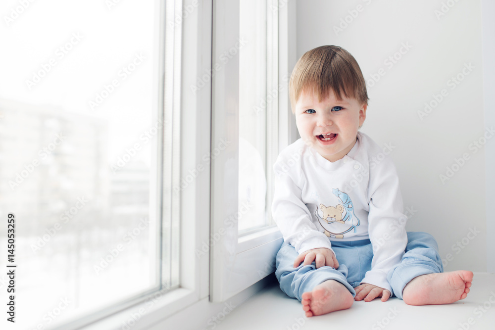 Adorable little baby seating on windowsill. look at the camera Adorable little baby seating on windowsill. look at the camera