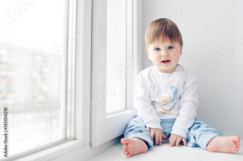 Adorable little baby seating on windowsill. look at the camera