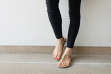 Close up of Bare Feet with Red Nail in Sandals and Black Jeans Woman On The Concrete Floor Background Great For Any Use.