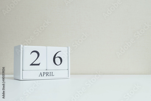 Closeup white wooden calendar with black 26 april word on blurred white wood desk and cream color wallpaper in room textured background with copy space in selective focus at the calendar