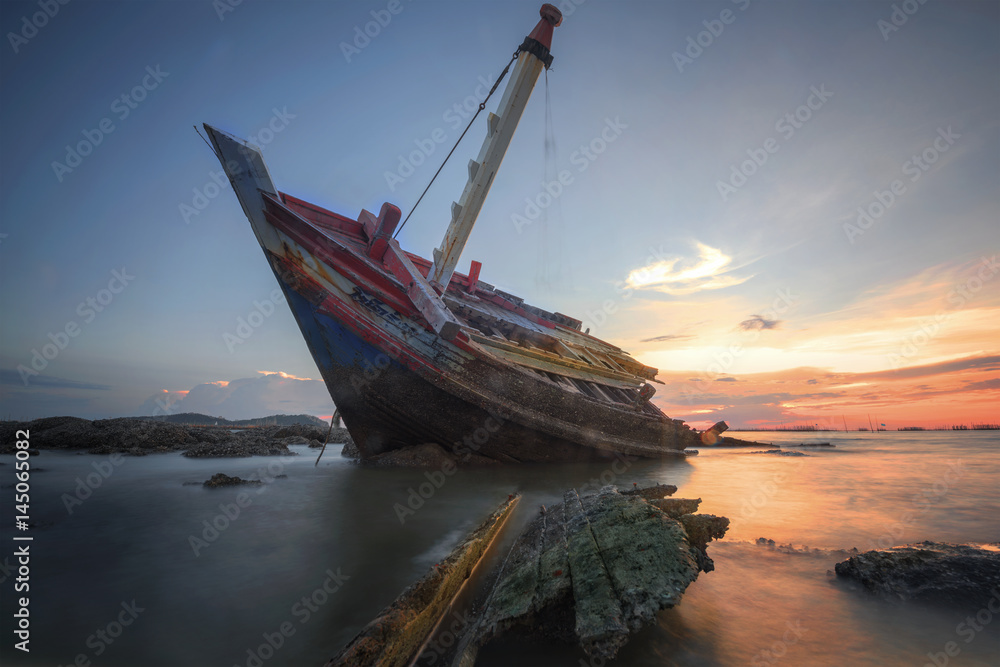 Boat deteriorate breaking down laying in the coast side with sunet in background