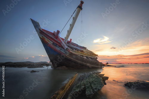 Boat deteriorate breaking down laying in the coast side with sunet in background © ID_Anuphon