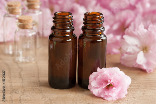 Two bottles of essential oil, with pink japanese cherry blossoms in the background